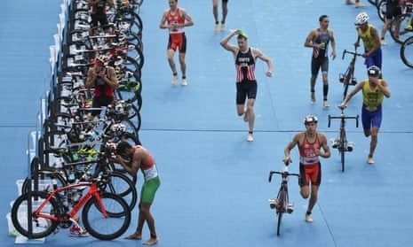 Triathleten laufen mit Fahrrädern durch eine blaue Wechselzone